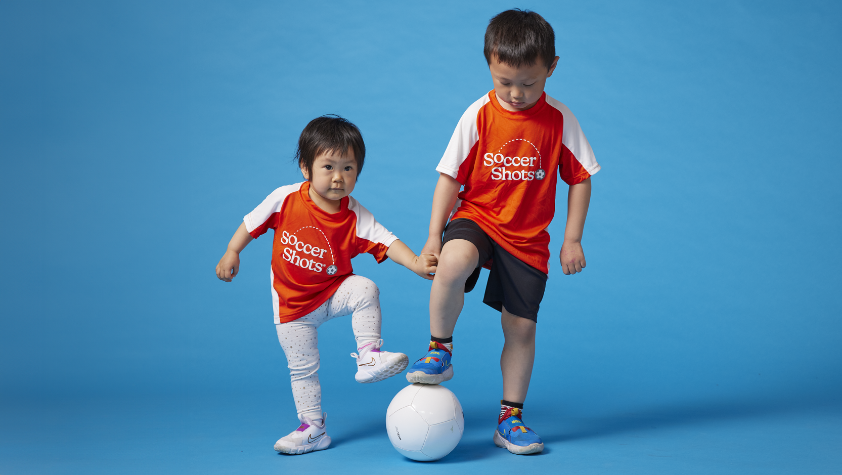 Little boy and girl in Soccer Shots jerseys with a soccer ball.